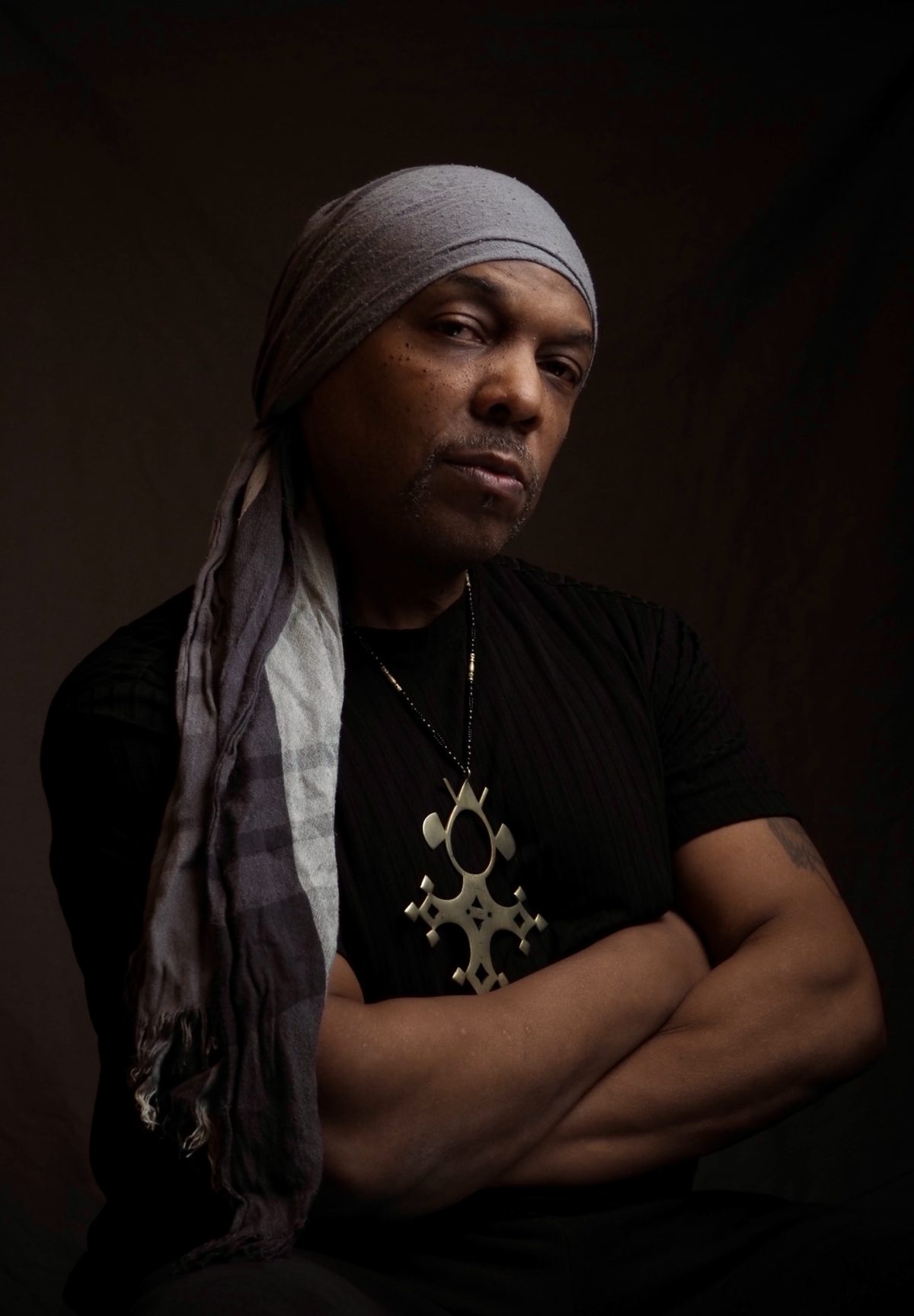 Portrait of Nuri Shakoor wearing a grey head wrap and a Tuareg cross pendant